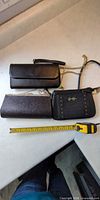 Three black evening purses with tape measure showing size