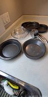 Assorted metal pie pans, glass pie plate, potato ricer on countertop