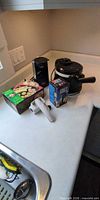 All four items on countertop: waffle maker, can opener, sushi maker box, cheese mill box