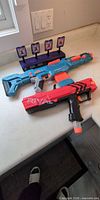 Blue/orange Elite blaster, red Rival blaster, purple electronic target on countertop
