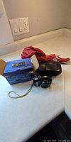 Camera with strap, camera case, Canon box and red umbrella on countertop
