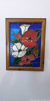 Framed stained glass panel with floral design against wall