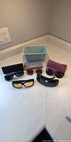 All five pairs of sunglasses, three cases, blue bin displayed on countertop