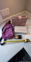 All items arranged on countertop: purple sling bag, pink pouch, white case, tin with brushes
