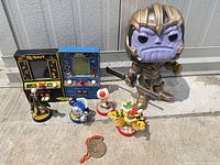 Group shot of all items including Thanos Funko Pop, two mini arcades, four Amiibos, coin