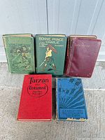Five antique books standing and lying on concrete surface showing covers and binding colours