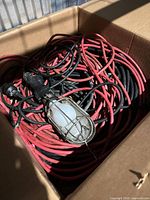 Box containing coiled red and black cables and a handheld caged work light
