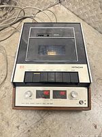 Front and top view showing transport lid, control buttons, VU meters and brand/model