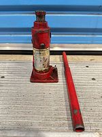 Full view of hydraulic bottle jack and handle on metal surface