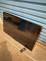 Front view of Insignia flat-panel TV leaning against wall with remote below