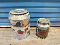 Large and small painted metal milk-can tins side by side