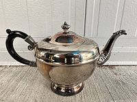 Right side view of silver-plated footed teapot showing handle, spout, pedestal base and lid