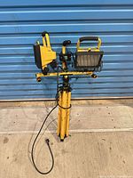Full view of folded yellow dual-head halogen work light on tripod with power cord