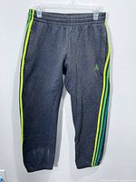 Full view of dark grey Adidas joggers hanging, showing stripes and tapered legs