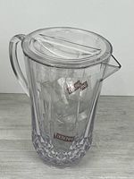 Front view of sealed clear plastic Dubonnet pitcher with cups visible inside