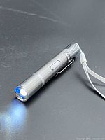 Flashlight powered on showing white beam and strap attached