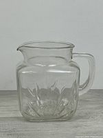 Front view of clear square glass pitcher showing handle, spout and starburst pattern