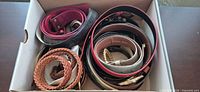 Box containing assorted belts showing variety of colours and materials