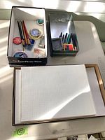 Overall view showing boxes with paper, pencils, pens, compass, erasers and pinback buttons