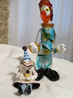 Both clown figurines: glass clown standing behind earthenware clown