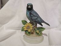 Front view of blue swallow tanager porcelain figurine on base with yellow flower