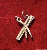 Front view of 10K gold scissors and comb pendant on red background
