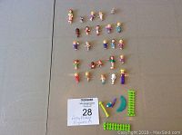 Full lot of 25 Polly Pocket figures and accessories laid out on grey surface, with auction tag #28 visible.