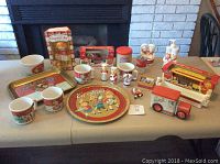Full view of the Campbell's Soup collection including mugs, doll, tray, tins, banks, and kitchen items on table.
