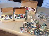 Photo showing three boxes of assorted baseball and hockey cards, with loose cards and a bag of plastic cased cards scattered on the table