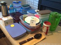 Photo of various plastic storage bowls and containers, pitcher, cake carrier, salad utensils, and other kitchenware on table.