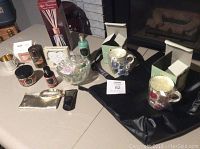 Various giftable items arranged on table including packaged mugs, bottles, candles, a black tote, and a gold pouch.