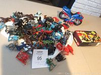 Photo showing LEGO motorbike toy and large group of plastic warrior toys scattered on a table with original box for the motorbike toy.