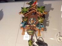 Front view of the cuckoo clock with leaves and birds painted on wooden frame, showing clock face and pendulum.