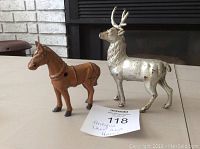 Photo showing both antique metal deer and horse figurines side by side with a paper label