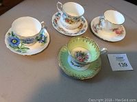 Four assorted teacups and saucers on a table, each with distinctive floral design and gold trim