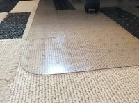 Clear plastic carpet protector mat laid flat on beige carpet showing rounded corners and traction dots underneath