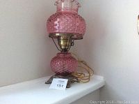 Side view of vintage pink hobnail glass hurricane lamp on a white shelf showing the lamp's pink glass textured base and chimney with brass hardware and cord.