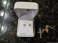 Pearl stud earrings in box beside chain with cross pendant
