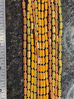 Close view of multiple strands showing yellow, orange, translucent lucite tube beads beside ruler for scale