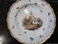Front of plate showing hand-painted scene, insects, gilt rim, crack line
