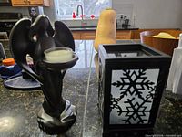 Resin angel-wing votive holder beside metal lantern showing snowflake panel