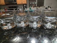 Front view of four clear heavy whiskey glasses showing bubble in base