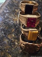 Stacked view of four gold men’s rings showing stones and signet top