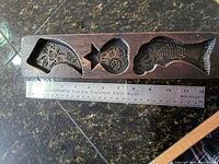 Full view of mold showing three carved cavities with ruler for scale