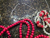 Rhinestone bracelet, red beads and cloisonné necklace on granite surface