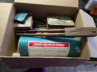 Overview of box contents showing solvent can, wood tool, tins and misc items