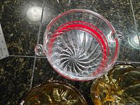 Top view of clear handled bowl showing red rings and spiral base, partial view of amber bowls