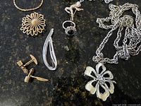 Close-up of left side items including chain necklace, daisy brooch, hair barrette, cufflinks and part of flower pendant