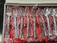 Flatware set in box showing forks and spoons in plastic sleeves