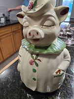 Front view of ceramic pig cookie jar displaying overall form, paint details and hat lid